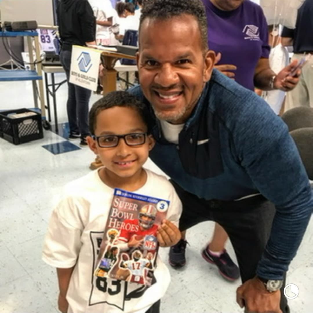 Andre Reed with a boy holding a Super Bowl Heroes book at a Boys & Girls Club