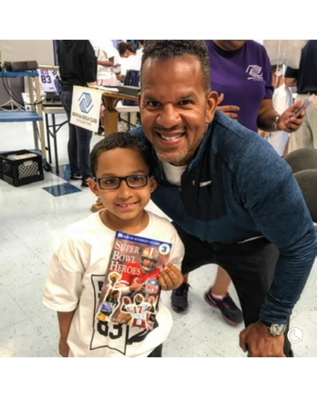 Andre Reed kneeling with a boy holding a "Super Bowl Heroes" reader at the Boys & Girls Club of Allentown