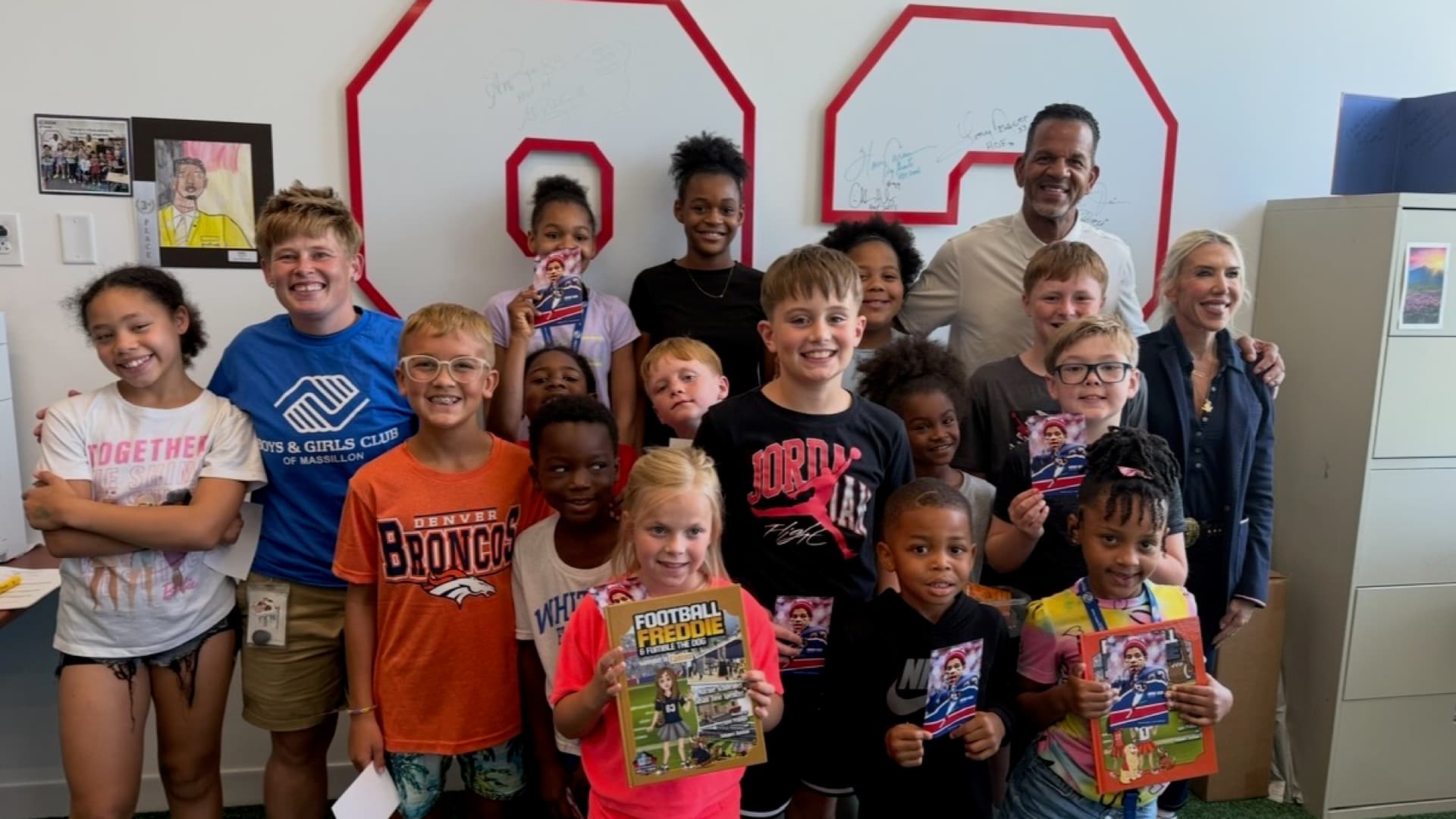 Andre Reed with a group of Read with Reed 83 kids in front of a signed #83 wall at a Boys & Girls Club