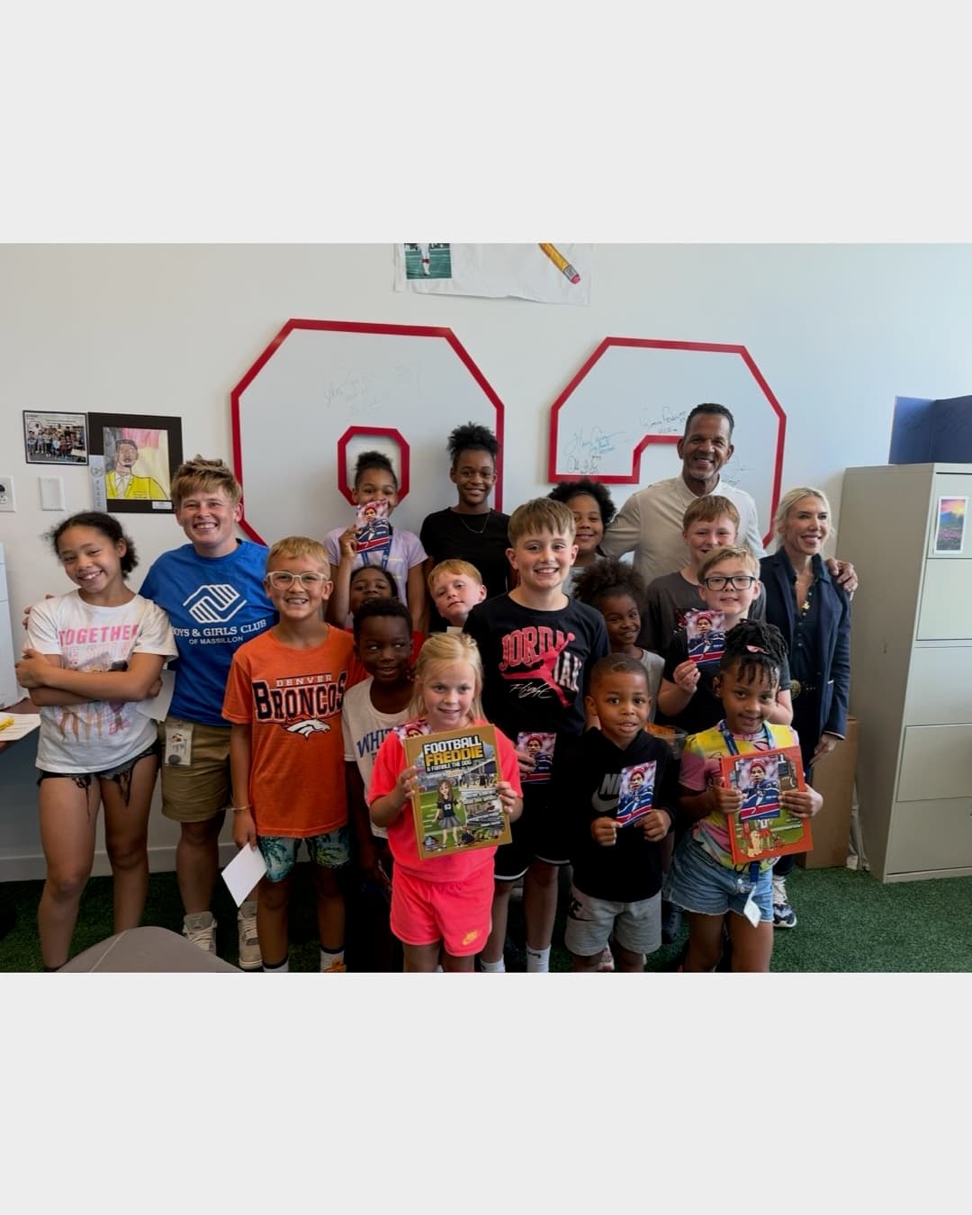 Andre Reed with a large group of kids holding "Football Frenzy" readers in front of the signed red 83 wall decal