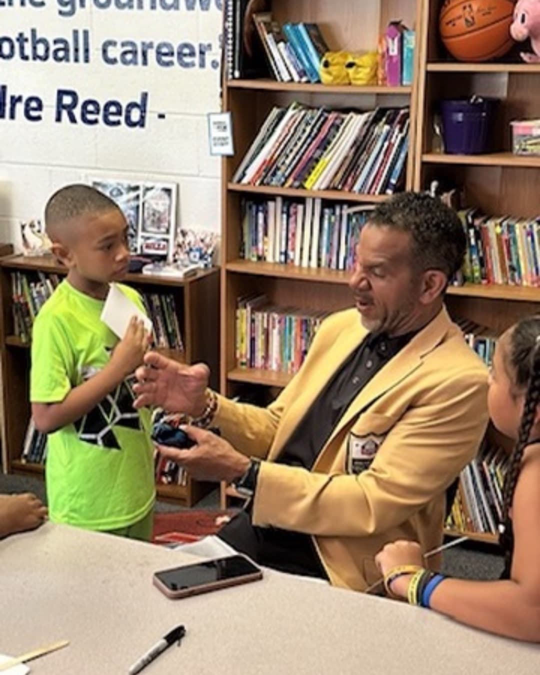 Andre Reed kneeling beside a young boy holding a stuffed toy at a Boys & Girls Club