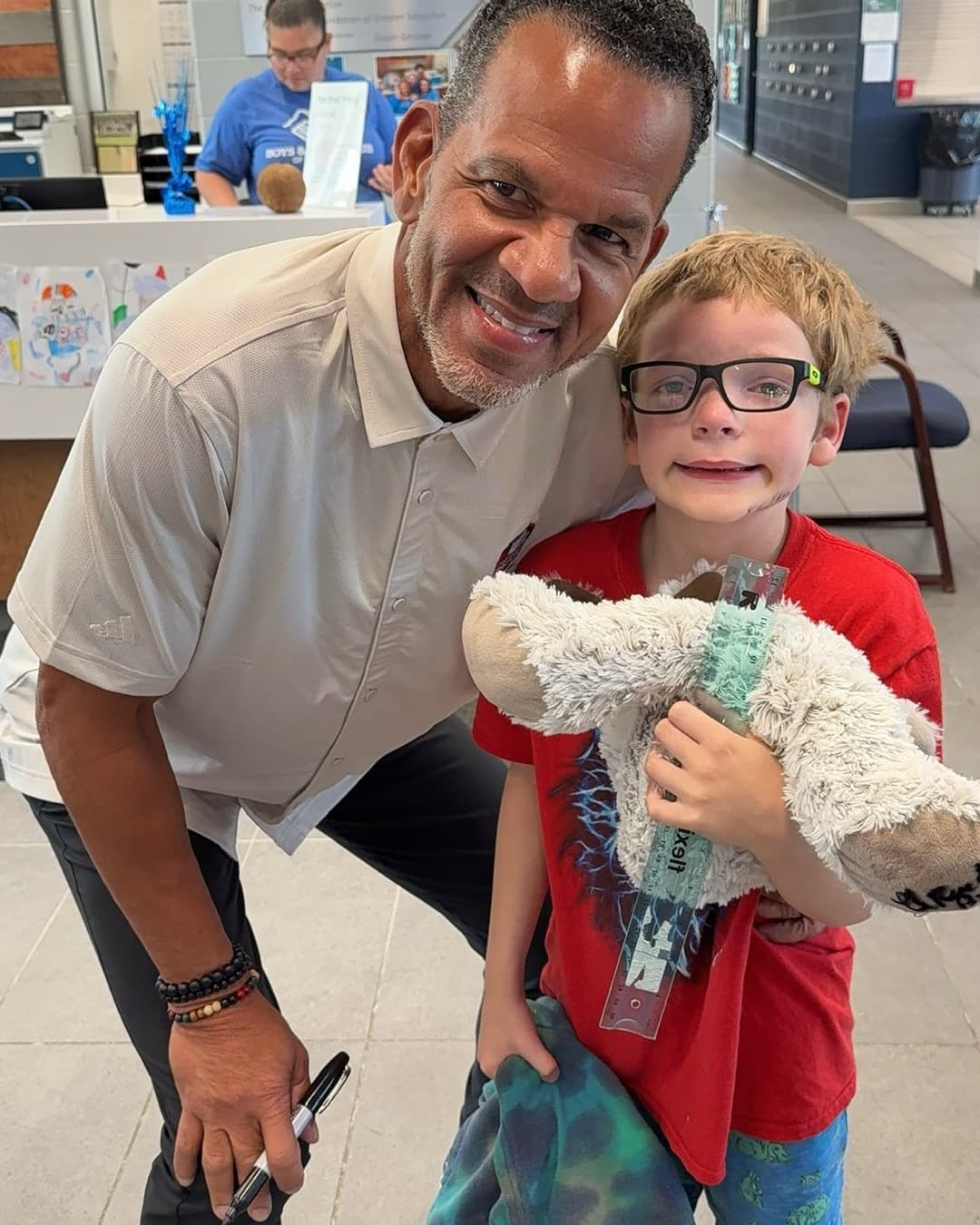 Andre Reed posing with a young boy holding a stuffed animal at the Boys & Girls Club of Massillon