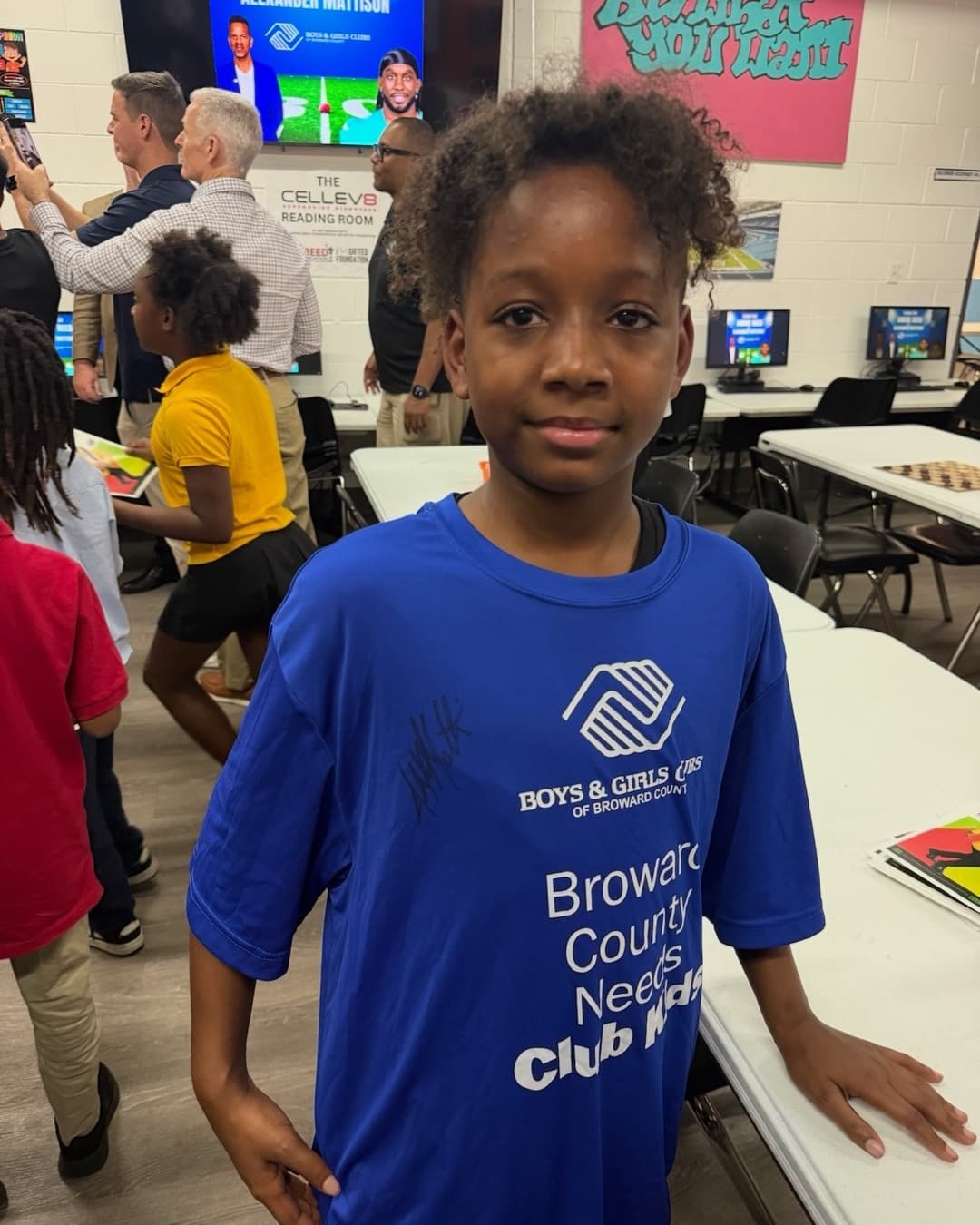 Boy in a signed BGCA Broward shirt smiles at a Read with Reed event