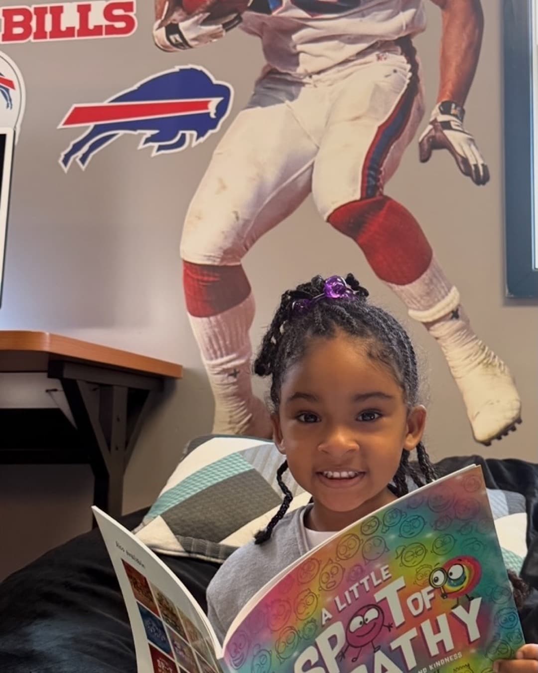A young girl smiling as she reads "A Little Spot of Empathy" beneath a life-size Andre Reed #83 Buffalo Bills wall decal