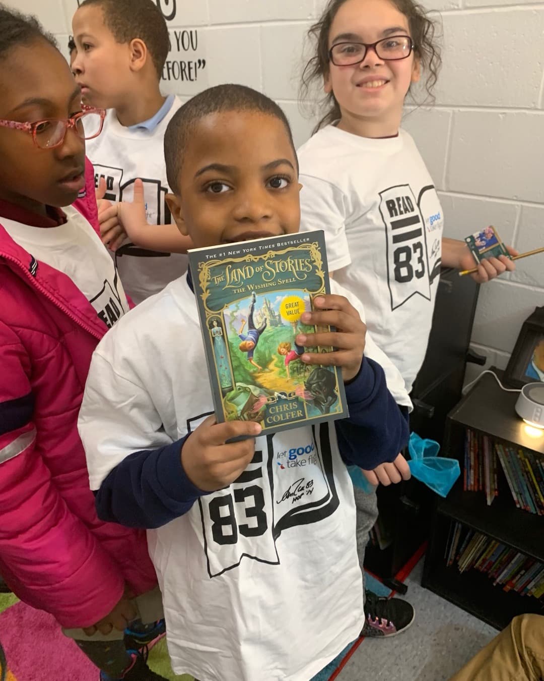 A boy holds up his copy of "The Land of Stories" in a Read with Reed reading room