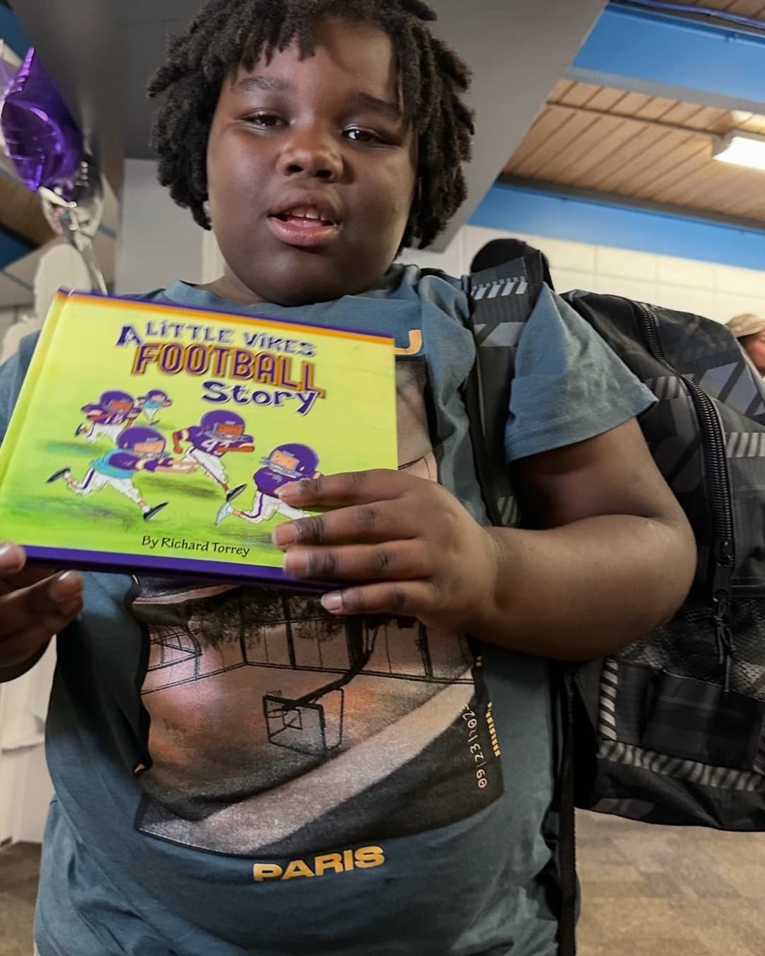 A young reader holding a 'Little Vikes' book at a Read with Reed reading room