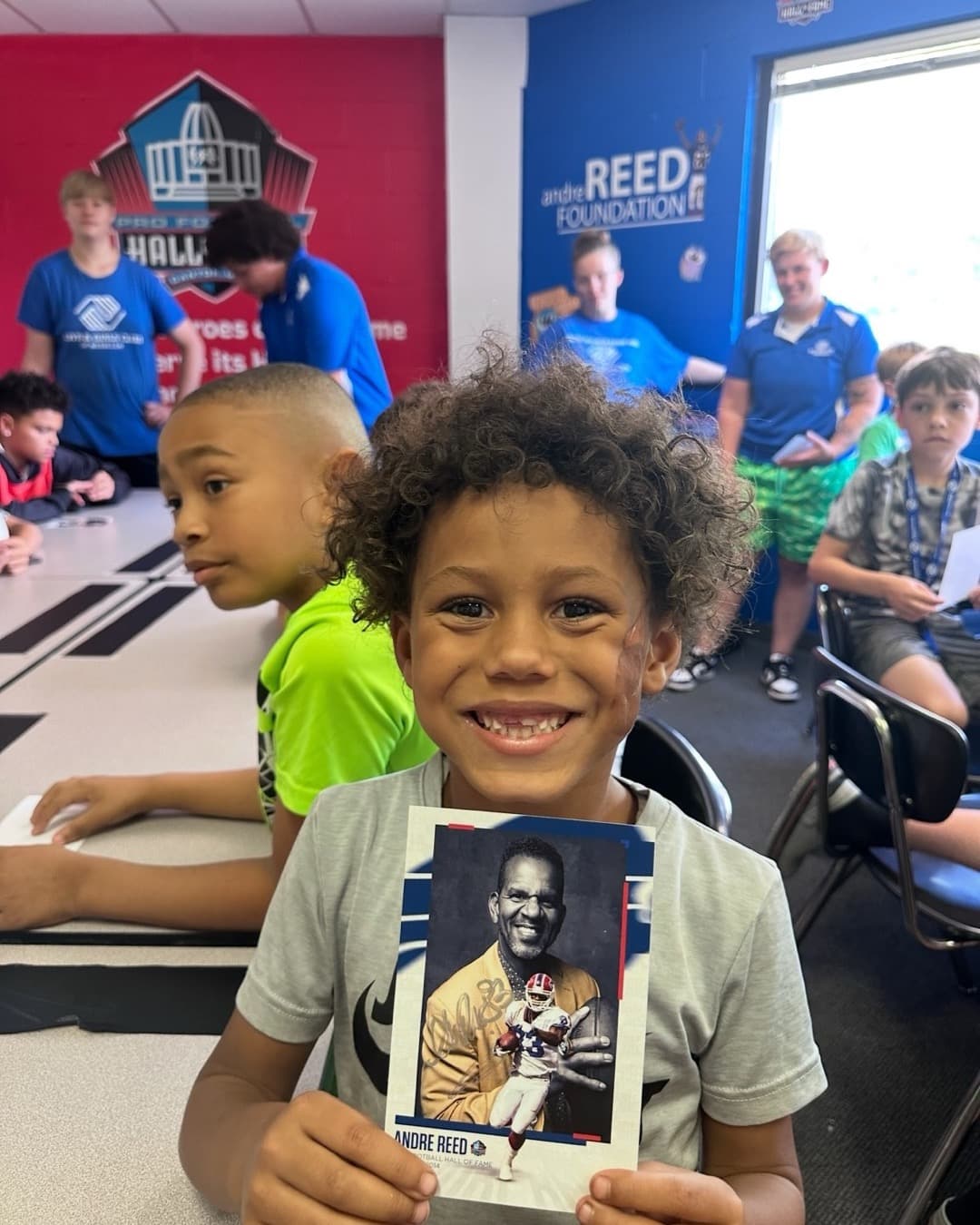 Andre Reed with a group of kids holding his signed Read 83 trading card at a Boys & Girls Club
