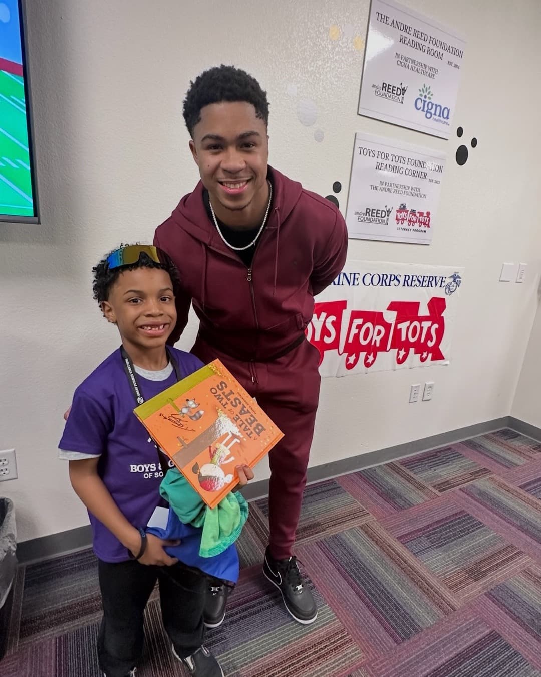 A teen volunteer hands a young child a book at a Read with Reed community giveaway