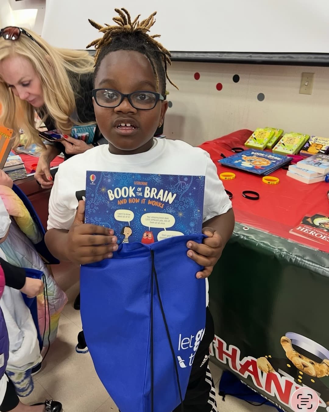 A girl in glasses proudly holding up "The Book of the Brain and How It Works" beside a table of donated books